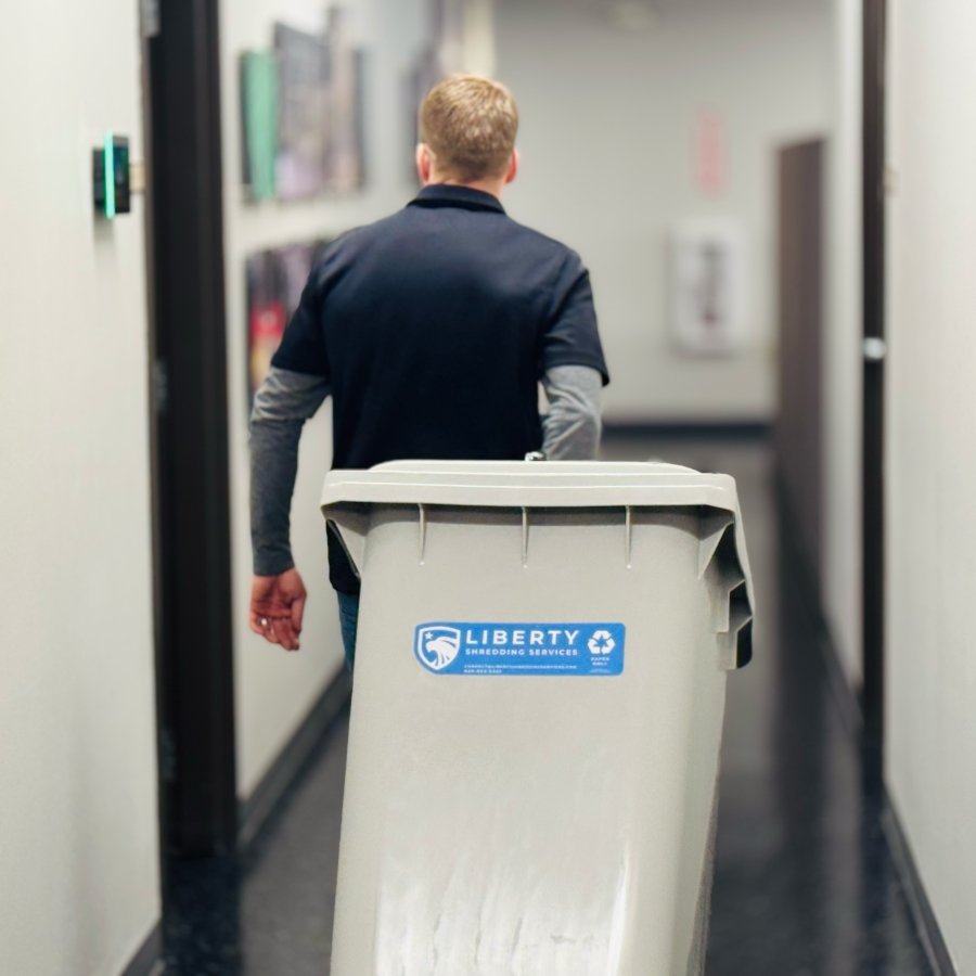 A person wheeling a locked shred bin though a hallway